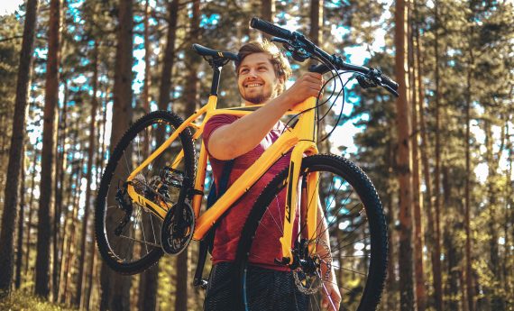Positive sporty male holding yellow mountain bicycle upper his head.