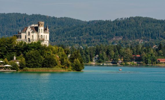 WORTHERSEE, AUSTRIA - AUGUST 08, 2018:  Great scenery from the boat to the shore line of the lake, beautiful buildings, mountains, forests, highways. Tourists who enjoy a variety of water recreation types.